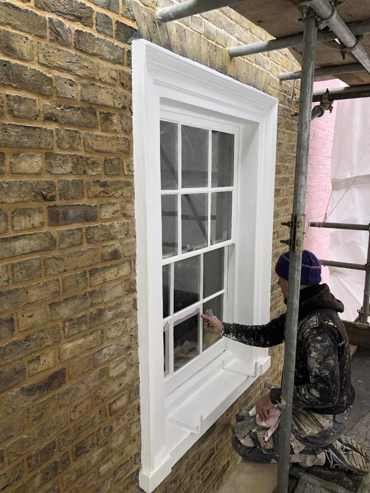 Decorator painting a sash window beside newly repointed brickwork